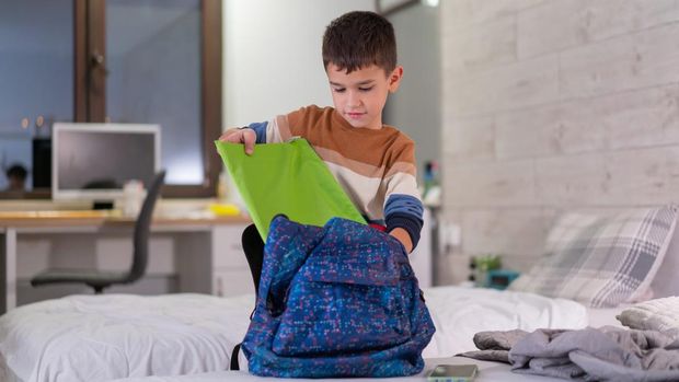 ilustrasi anak mandiri Schoolboy prepares his backpack for school standing in the room and preparing for school
