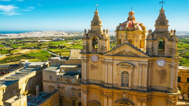 Kota Mdina The main church in Mdina city - old capital of Malta. Aerial nature landscape, sunny day, blue sly, winter, a lot of green grass, field on background. Malta country