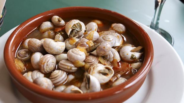 Makanan Spanyol Caracoles Traditional snail dish called caracoles served in a tapa bar next to a glass of red wine in Spain