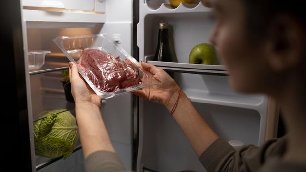 Ilustrasi seseorang menyimpan daging mentah ke dalam kulkas/Foto: Magnific/magnific Tps marinasi daging sapi agar bumbu meresap