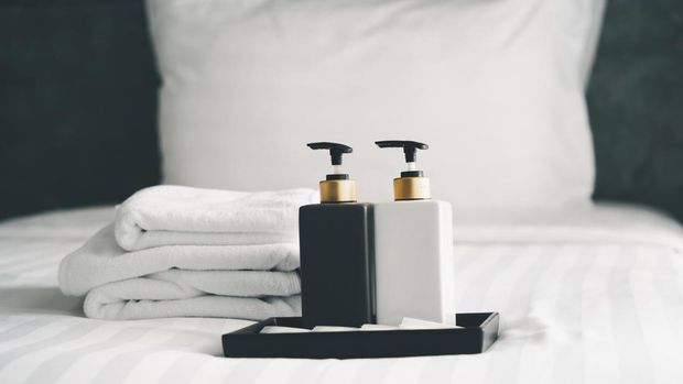 bottles of bathroom accessories on white cleaned bed in hotel bedroom, in soft focus