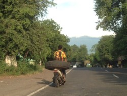Gokil, Pria Ini Mengendarai Motor Sambil Duduk di Ban Truk Besar
