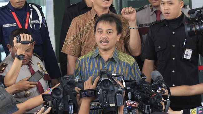 Tersangka Roy Suryo menunjukkan bahasa isyarat saat digiring polisi ke Gedung Direktorat Tahanan dan Barang Bukti Polda Metro Jaya.