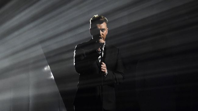 Dengan memadukan sepatu high heels, kemeja berbahan lace, dan tuksedo klasik serba hitam, Sam Smith melenggang percaya diri.
