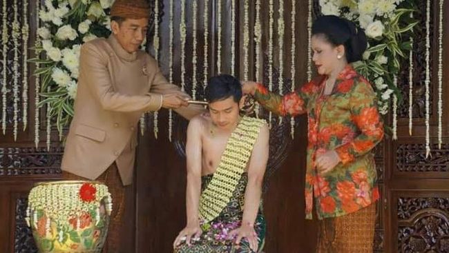 Dengan menggunakan beskap cokelat dan blangkon cokelat, wajah Jokowi terlihat tegang dan agak kaku ketika menyiramkan air siraman ke leher sang putra.