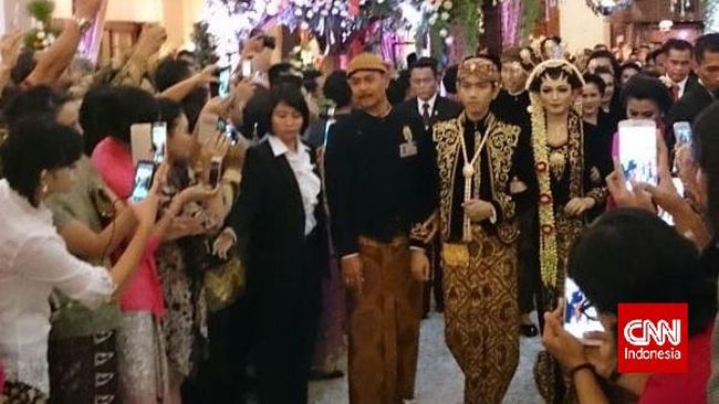 Dibelakangnya, Joko Widodo didampingi oleh Iriana berjalan mengenakan pakaian berwarna senada dengan bawahan kain truntum.