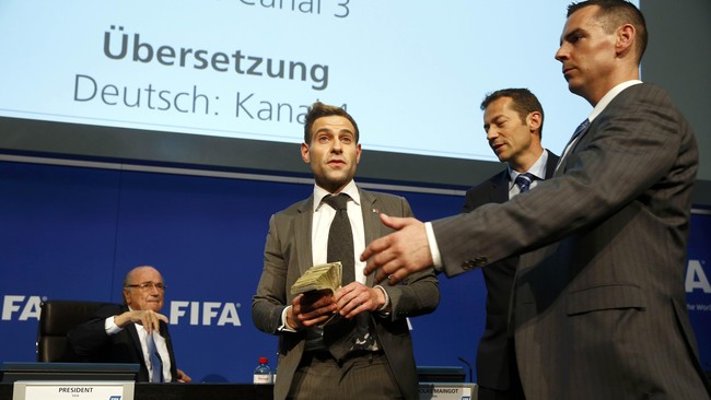 Komedian Inggris melemparkan gepokan uang dolar palsu ke arah Presiden FIFA Sepp Blatter dan menyebut hal itu dari Korea Utara agar jadi tuan rumah Piala Dunia.