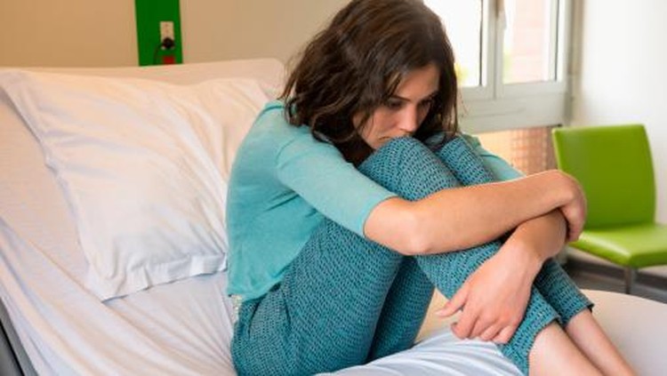 Female depressed patient sitting on the bed in a hospital ward