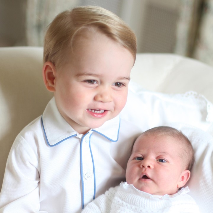 <p>Ini Putri Charlotte saat bayi sedang dipangku kakaknya. Sama kan bajunya dengan yang dipakai adiknya? Kemungkinan besar, Putri Charlotte melungsurkan ke adik bayinya. (Foto: Getty Images)</p>