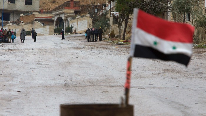 A Syrian national flag flutters near residents who said they have received permission from the Syrian government to leave the besieged town as they wait with their belongings after an aid convoy entered Madaya, Syria, January 14, 2016. Aid was sent on Thursday to the Syrian town blockaded by pro-government forces and two villages besieged by rebels for the second time this week, and a U.N. official said he hoped to make more deliveries to areas where people are starving. Dozens of trucks left Damascus for the town of Madaya at the Lebanese border, and the two villages of Kefraya and al-Foua in rebel-held Idlib province. Tens of thousands of people have been trapped in the areas for months. REUTERS/Omar Sanadiki