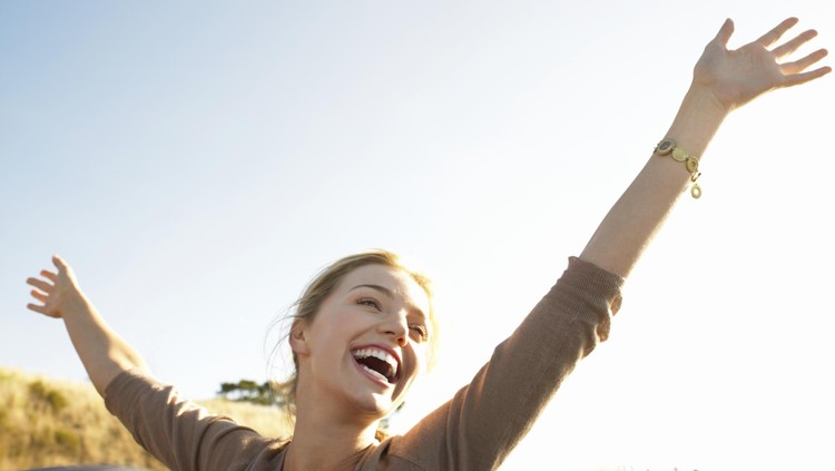 Young Woman Sits in the Back of a Convertible, Her Arms in the Air, Laughing With Joy