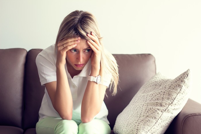 Sad young woman sitting on couch in depression.