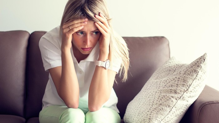 Sad young woman sitting on couch in depression.