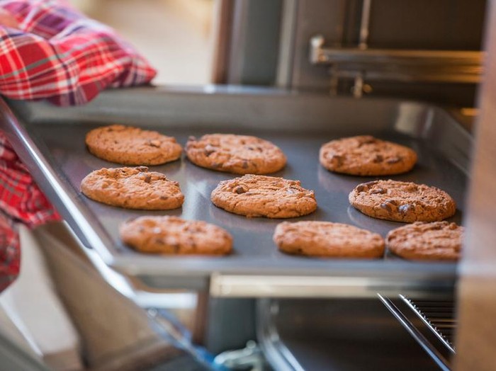 Cropped image of hand removing cookie tray from oven in kitchen
