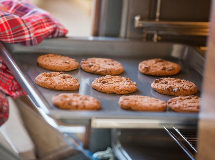 Cropped image of hand removing cookie tray from oven in kitchen