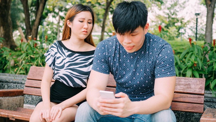 Ilustrasi Pasangan Selingkuh Jealous girlfriend peeking and spying her boyfriend mobile phone while he is reading a message