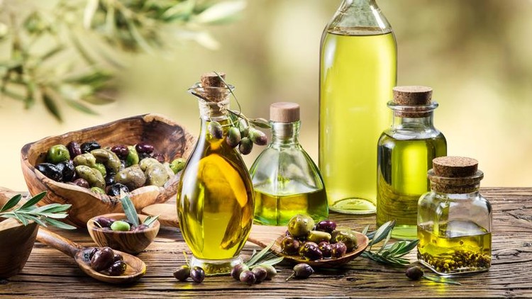 Olive oil and berries are on the wooden table under the olive tree.