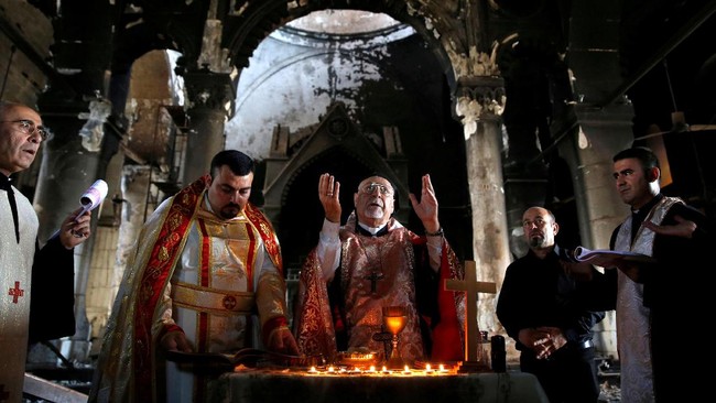 Dikelilingi dinding hangus, di hadapan altar yang hancur, puluhan warga Kristen Irak mengadakan misa di Gereja Konsepsi Imakulasi di Qaraqosh pada Minggu.
