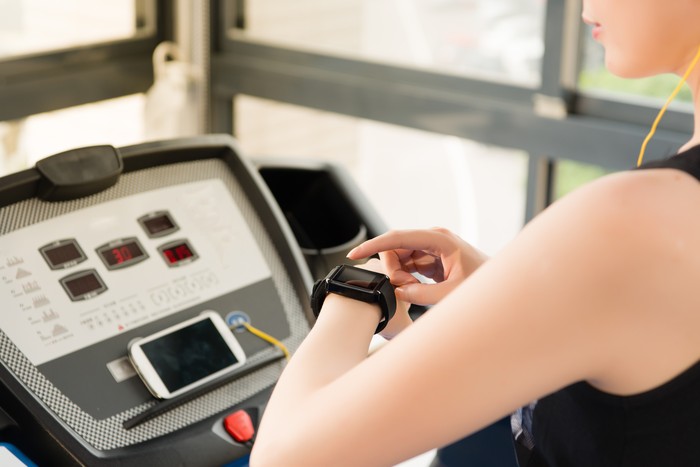 sport asian woman running treadmill use smartwatch connect smartphone listening music. indoors gym background. health sport concept