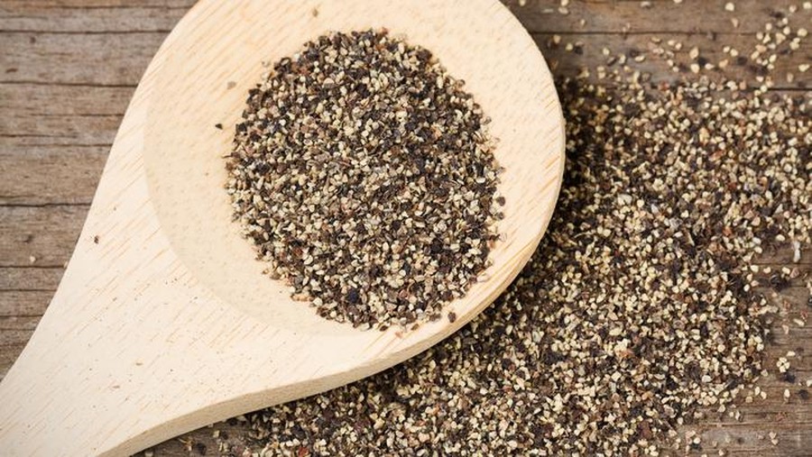 Coarse ground black pepper on a wooden spoon and spilled on an old, weathered wood surface.