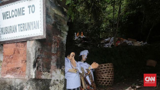 Pintu masuk makam di pemakaman Desa Trunyan.  Ada boneka yang di bikin oleh masyarakat Trunyan untuk meyambut wisatawan dan juga ada sebuah pohon besar bernama Taru Menyan yang tumbuh lebat di pintu masuk pemakaman. Pohon ini dipercaya mampu menghilangkan bau busuk yang ditimbulkan oleh jenazah. Konon, pohon ini juga menjadi asal usul terciptanya desa. CNN Indonesia/ Andry Novelino