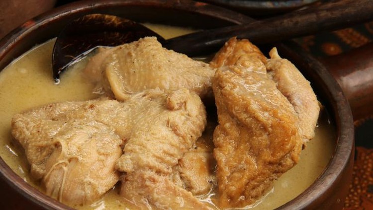 Opor Ayam, the Javanese white chicken curry, popularly served in various Javanese meal dishes, including Gudeg Jogja. The dish is served in an earthenware pot with a wooden ladle inserted further back. The pot is placed on table covered with Javanese batik table cloth.