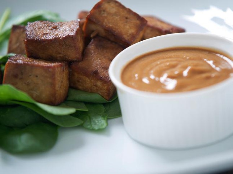 tahu bacem Indonesian marinaded tofu with peanut satay sauce on a small bed of spinach.