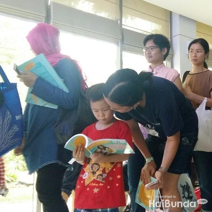 <p>Sambil mengantre tanda tangan, ada anak yang kepo sama bukunya. Isinya apa hayo, Nak?</p>