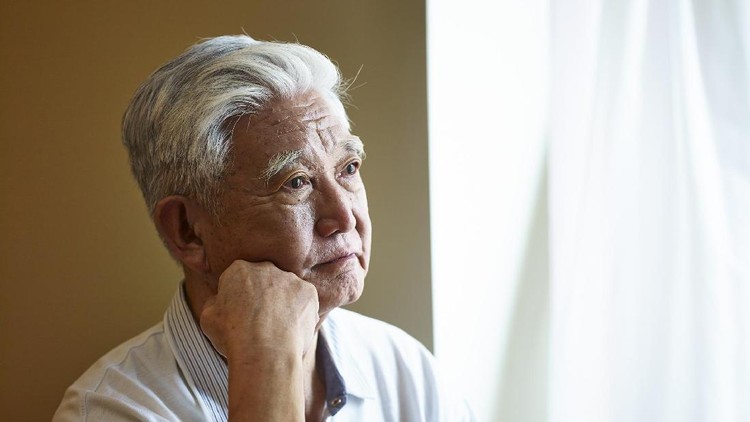 portrait of a sad asian senior man sitting by the window hand on chin.