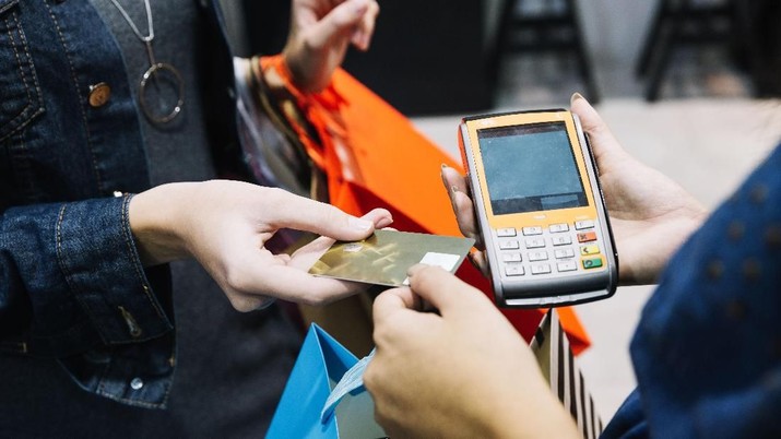 Close-up of female hand holding smartphone. Young businesswoman sitting at laptop in office holding credit card and entering data on her mobile phone