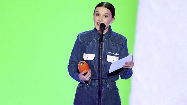 Aktris Stranger Things, Millie Bobby Brown mengenakan baju yang memuat kepeduliannya akan aksi anti senjata saat hadir di Nickledeon Kids Choice Awards 2018.