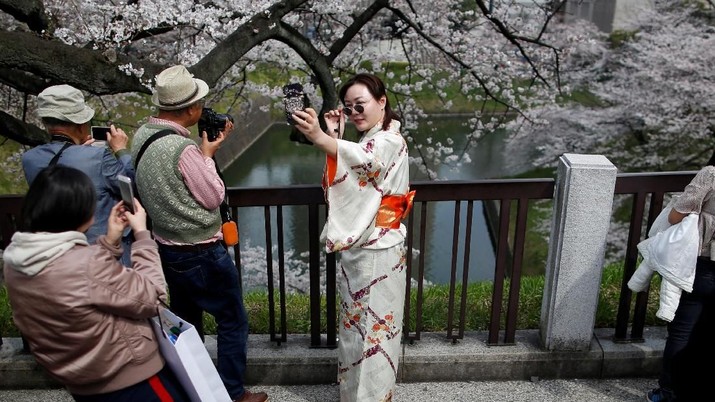 Seorang wanita berbaju kimono mengambil foto selfie di parit Chidorigafuchi, saat pengunjung menikmati bunga sakura yang mekar sepenuhnya, selama musim semi di Tokyo, Jepang 26 Maret 2018. REUTERS / Issei Kato