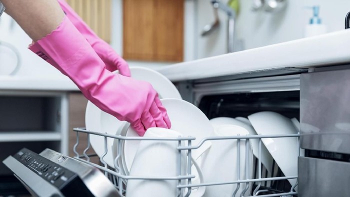 housewife taking out clean dishware from dishwasher at home kitchen
