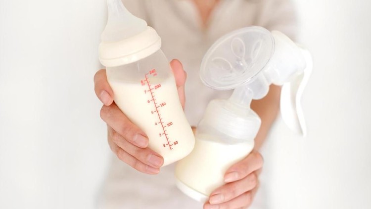 Breast pump and bottle with milk in woman's hand in blurred background