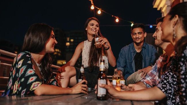 Group of happy young people having a rooftop party at evening. Friends enjoying party with drinks.