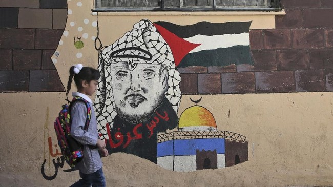 A child walks in front of a mural painting depicting the late Palestinian leader Yasser Arafat on her way to a school run by United Nations Agency for Palestinian Refugees (UNRWA) in Balata refugee camp, east of Nablus in the occupied West Bank on August 29, 2018, on the first day of classes after the summer holidays. 
US President Donald Trump cut of more than $200 million in aid for Gaza and the West Bank this month after earlier freezing of $300 million in annual funding for the UNRWA. / AFP PHOTO / Jaafar ASHTIYEH