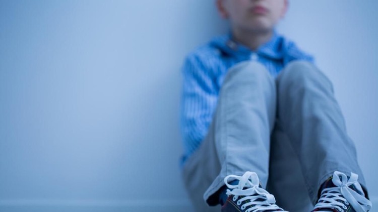 Sad boy in sneakers with asperger's syndrome sits alone in his room