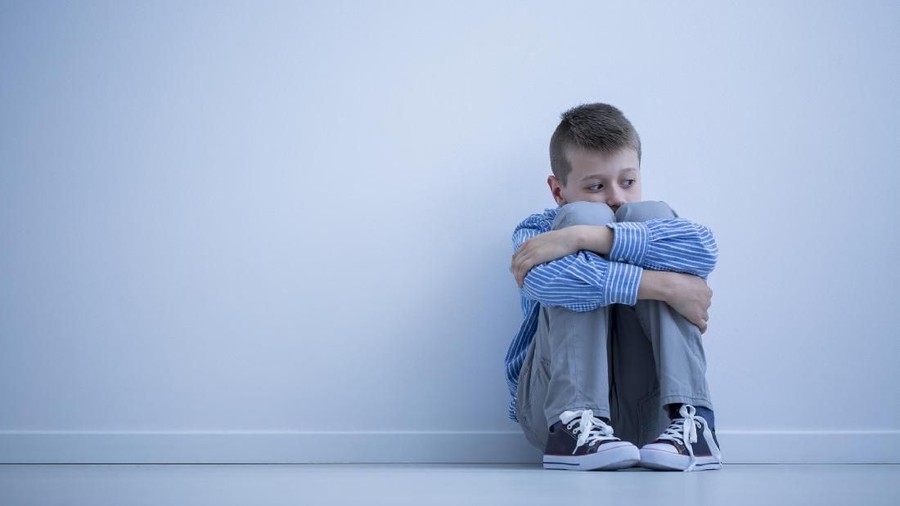 Young boy with hypersensitivity sitting alone on the floor against the wall with copy space