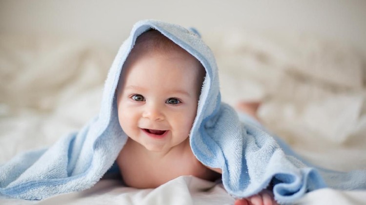 Cute little baby boy, relaxing in bed after bath, smiling happily, daytime