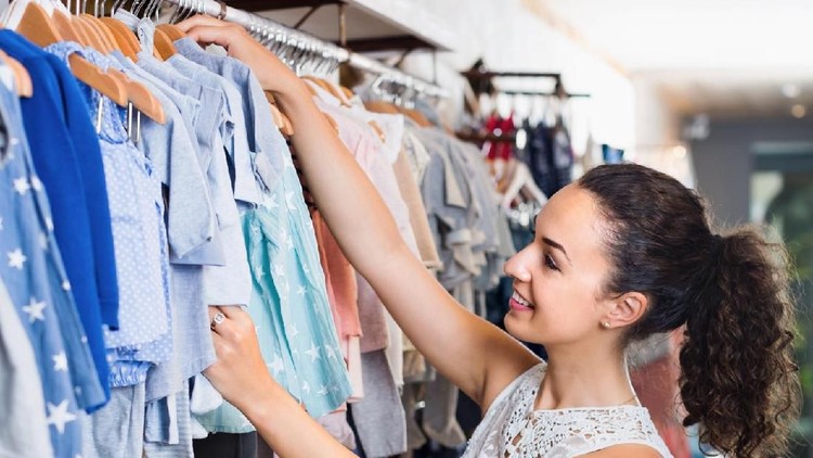 Young cheerful woman choosing blue baby clothes in kids apparel boutique