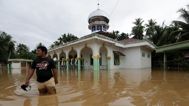 Warga berjalan melintasi banjir di depan sebuah masjid akibat luapan Sungai Teunom di Blang Baro, Aceh Jaya, Aceh, Selasa (16/10/2018). Luapan air Sungai Teunom dan tiga sungai lainnya mengakibatkan tujuh kecamatan digenangi banjir hingga ketingggian 1,5 meter di Kabupaten Aceh Jaya. ANTARA FOTO/Irwansyah Putra/wsj.