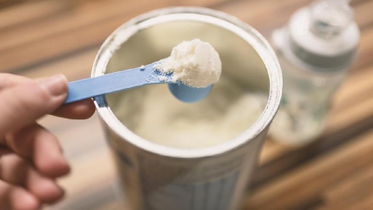 Susu Bubuk Powder milk for baby and blue spoon on light background close-up. Milk powder for baby in measuring spoon on can. Powdered milk with spoon for baby. Baby Milk Formula and Baby Bottles. Baby milk formula on kitchen background