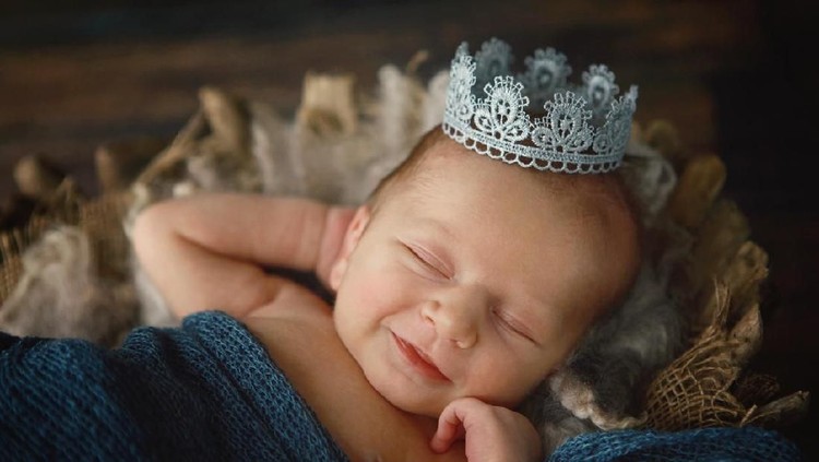 A newborn baby boy smiles as he wears a silver crown. A prince is born!