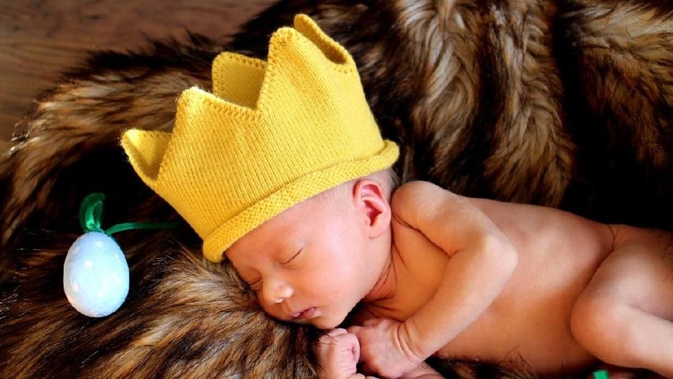 A newborn baby boy smiles as he wears a silver crown. A prince is born!