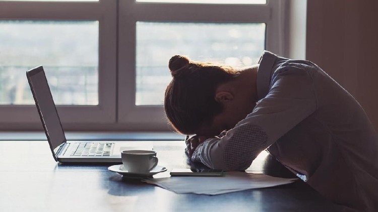 An exhausted customer service rep snoozing on her computer with her hand still clutched to her coffee.