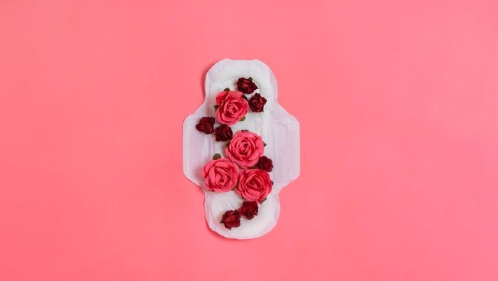 White sanitary pad with red and pink flowers on it, woman health or body positive concept. Pink background.  Flatlay. Copyspace