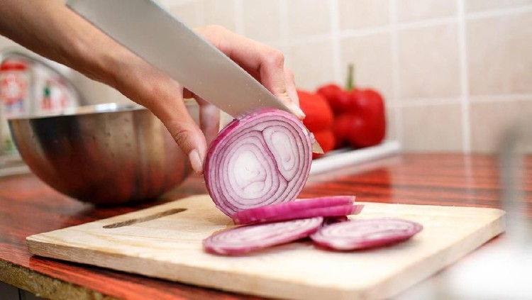 Woman's hand cut red onions on cutting board in home kitchen