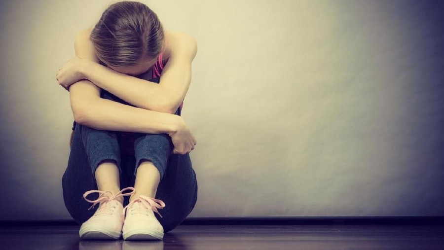 Sad depressed young teenage girl sitting by wall hiding face. School, adolescence, home violence, unwanted love problems.