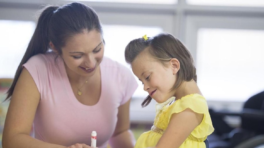 A caregiver is a helping a disabled girl with a coloring project at school.