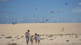 Seorang perempuan berjalan dengan anak-anaknya di tengah Festival Internasional Layang-layang ke-XXXI yang dihadiri sekitar 450 penerbang layang-layang profesional dari seluruh dunia di Pulau Canaria, Spanyol. (AFP/Desiree Martin)
